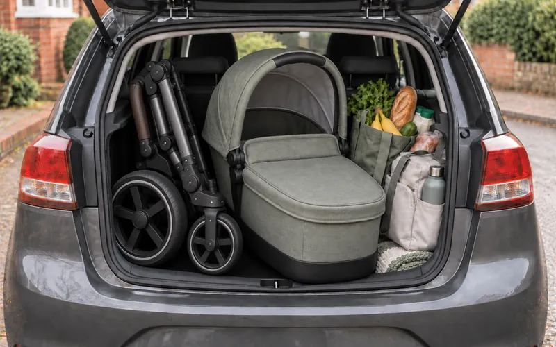 A folded pushchair chassis and carrycot in a car boot alongside shopping bags